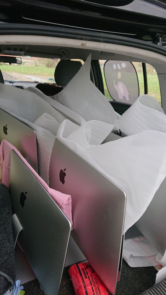 Das Bild zeigt den offenen Kofferraum eines Autos, der mit knapp zehn großen Rechnern von Apple beladen ist. Die Geräte sind gepolstert und fertig zum Transport.